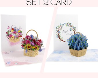 May include: Set of two pop-up greeting cards. One card features a basket of colorful flowers, the other a basket of blue flowers with the text "Forget me not". Both cards have a basket design.