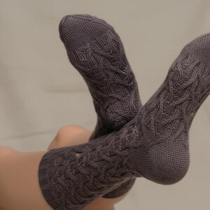 May include: A pair of grey cable knit socks. The socks have a textured cable knit pattern and are made of a soft material. These socks are designed to be worn on the feet and legs.