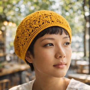 May include: Mustard yellow crochet beret. The beret features an open, floral-like pattern. The hat is worn by a person with short, dark hair and a white shirt. The background is blurred, with hints of greenery and a cafe setting.