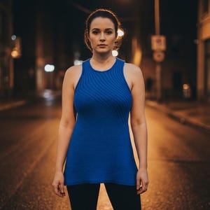 May include: A woman in a royal blue vest top and black leggings stands on a city street at night. The top has a ribbed texture. The background is blurred with streetlights and buildings, creating a dark atmosphere.