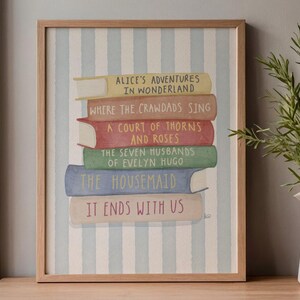 May include: A framed print depicting a stack of books with titles including "Alice's Adventures in Wonderland" and "It Ends With Us." The books are set against a striped background within a wooden frame, evoking a literary theme.