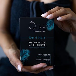 Pode incluir: Uma caixa preta de adesivos capilares "Nutri Hair" antiqueda é exibida em um fundo escuro. A caixa apresenta a marca "ODE COSMÉTIQUES" e um design estilizado de folhas de palmeira. O texto indica que é um adesivo fortificante integral para todos os tipos de cabelo.