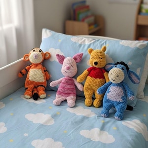 Könnte beinhalten: Vier handgefertigte gehäkelte Stofftiere, die Tigger, Ferkel, Winnie Puuh und I-Aah darstellen. Tigger ist orange mit schwarzen Streifen, Ferkel ist rosa, Winnie Puuh ist gelb mit einem roten Oberteil und I-Aah ist blau mit einem hellvioletten Bauch.