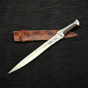 May include: A silver dagger with an engraved blade and a dark wood handle. The blade has an intricate design and the handle is adorned with silver accents. A brown leather sheath is included.