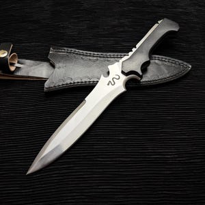 May include: A black and silver dagger with a leather sheath. The dagger has a curved blade and a black handle with a snake design.
