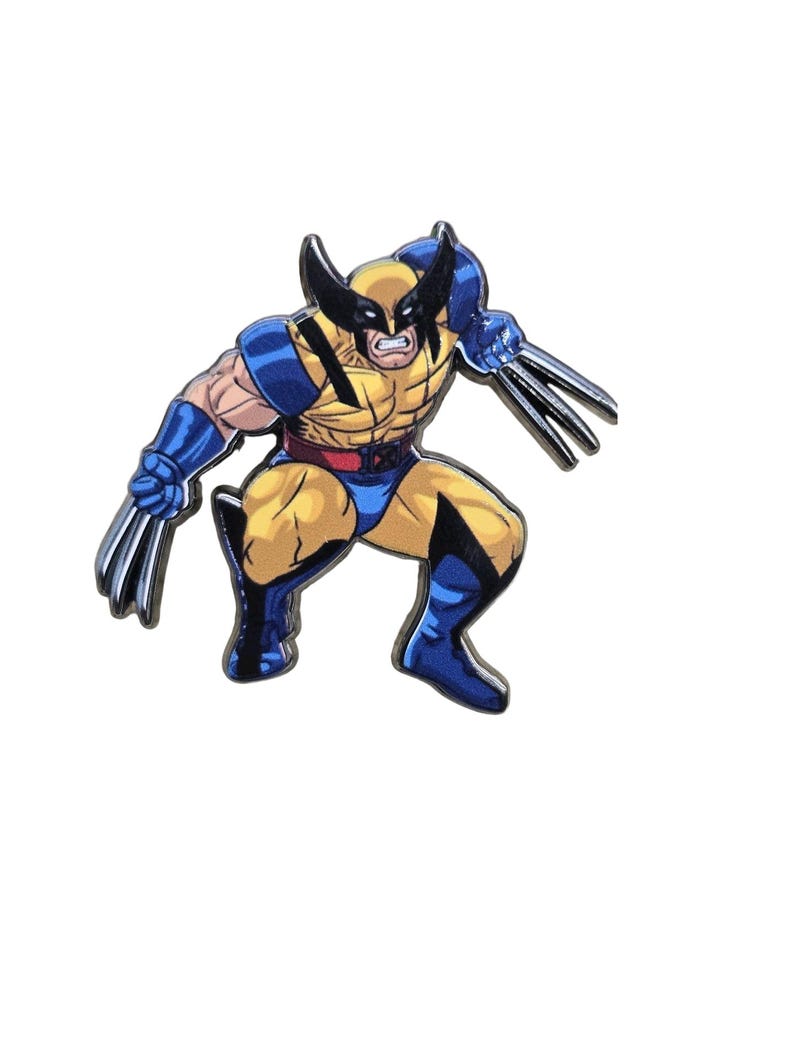 May include: A metal enamel pin featuring a comic book character in a crouching pose, wearing a yellow and blue suit with a black mask and pointed ears. The character has three silver-colored metal claws extending from each hand.