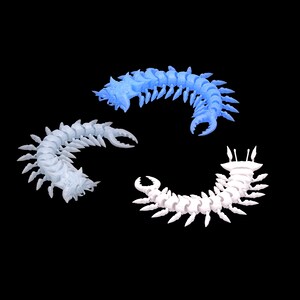 Puede incluir: Tres esculturas articuladas, segmentadas, con forma de insecto en tonos azules y blancos se disponen sobre un fondo negro. Cada una tiene un cuerpo curvado con múltiples patas y un apéndice en forma de garra en la cabeza. Las esculturas parecen estar impresas en 3D.