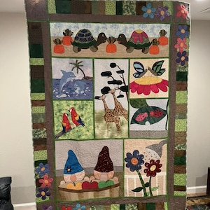 May include: A colorful patchwork quilt with various animal and nature scenes. The quilt features a turtle, a dolphin, a giraffe, a butterfly, a ladybug, and two gnomes. The quilt is made with a variety of fabrics and colors, including green, brown, red, blue, and yellow.