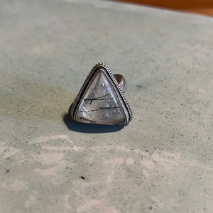 May include: A silver ring with a triangular clear quartz stone with black inclusions.
