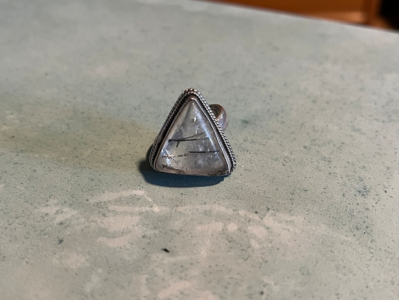 May include: A silver ring with a triangular clear quartz stone with black inclusions.