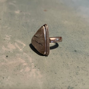 May include: A silver ring with a triangular shaped stone set in the center. The stone is clear with black lines running through it.