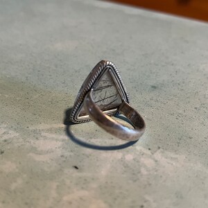 May include: Silver ring with a triangular shaped stone. The stone is a light gray color and has a textured surface.