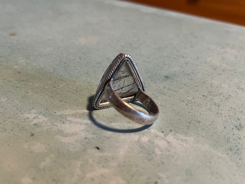 May include: Silver ring with a triangular shaped stone. The stone is a light gray color and has a textured surface.