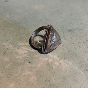 May include: A silver ring with a triangular clear quartz stone with black inclusions. The ring has a beaded edge.