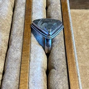 May include: A silver ring with a triangular grey and white gemstone set in a silver bezel. The ring is in a ring box.