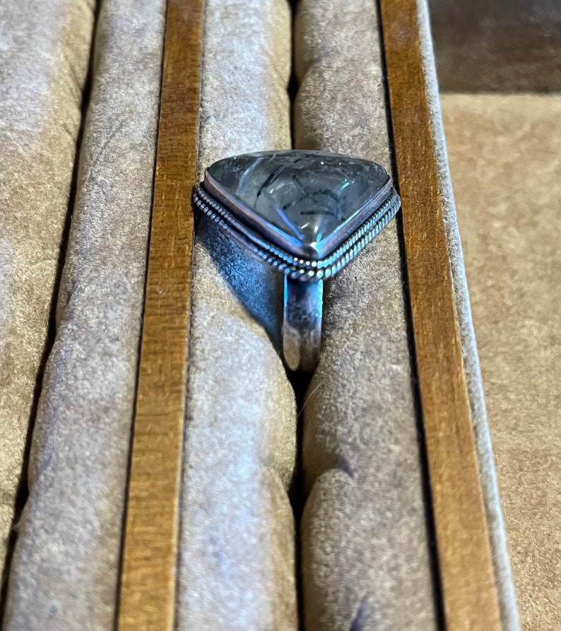 May include: A silver ring with a triangular grey and white gemstone set in a silver bezel. The ring is in a ring box.