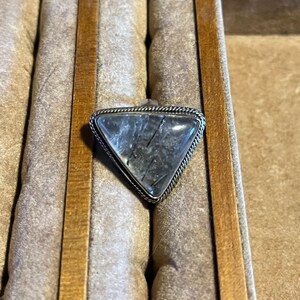 May include: A silver ring with a triangular clear quartz stone with black inclusions. The ring is in a wooden ring box.