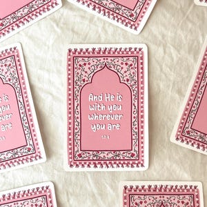 May include: Pink and black decorative card with a floral border and an arched opening. The card features the text "And He is with you wherever you are 57:4".
