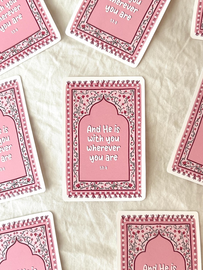 May include: Pink and black decorative card with a floral border and an arched opening. The card features the text "And He is with you wherever you are 57:4".