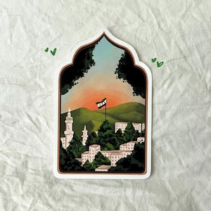May include: A sticker featuring a white archway design, showcasing a cityscape with a green hill and a flag with red, white, and black stripes. The cityscape is composed of white buildings with green trees in the foreground.