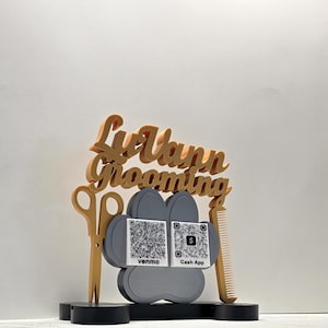 May include: A decorative sign for a pet grooming business. The sign features a paw print design with QR codes for Venmo and Cash App. The sign also includes scissors, a comb, and the business name "Liv Vann Grooming" in a stylized font.