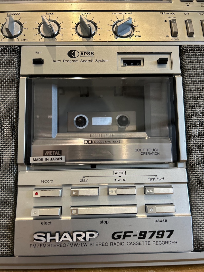 May include: Silver Sharp GF-9797 radio cassette recorder with a cassette tape inside. Features include balance, bass, treble, and record level controls. Includes APSS, Dolby System, and Soft-Touch Operation. Made in Japan.