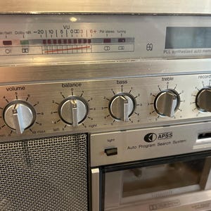 May include: Silver vintage stereo receiver with dials for volume, balance, bass, treble, and record level. Includes a VU meter, FM stereo tuning, and an auto program search system. The faceplate has a brushed metal finish.