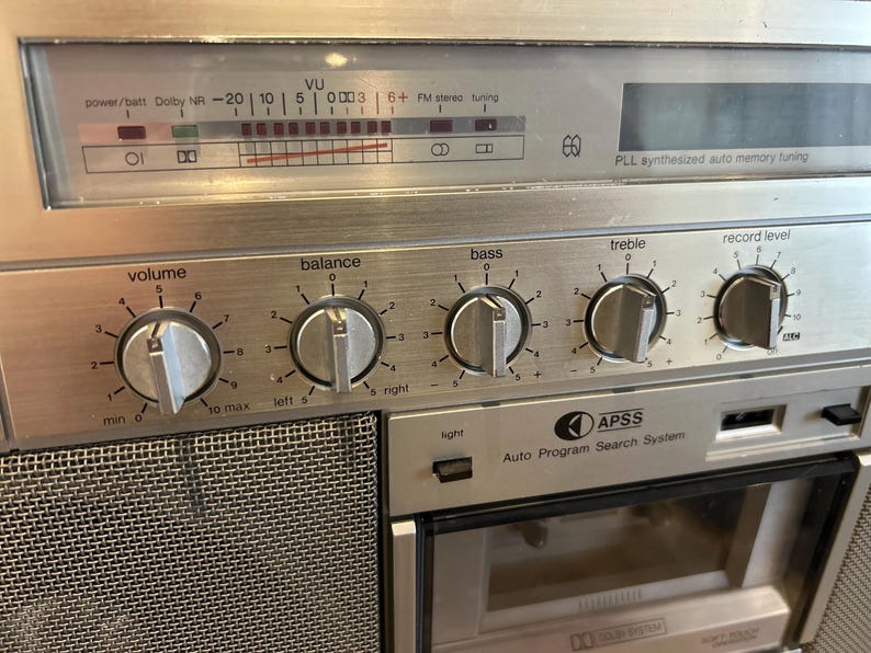 May include: Silver vintage stereo receiver with dials for volume, balance, bass, treble, and record level. Includes a VU meter, FM stereo tuning, and an auto program search system. The faceplate has a brushed metal finish.