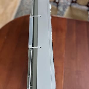 Pu&ograve; includere: Un lettore radio-cassette portatile color argento e grigio visto di lato, dotato di un'antenna metallica retrattile, una robusta maniglia per il trasporto e un involucro rettangolare in plastica con comandi laterali e una griglia per altoparlante.