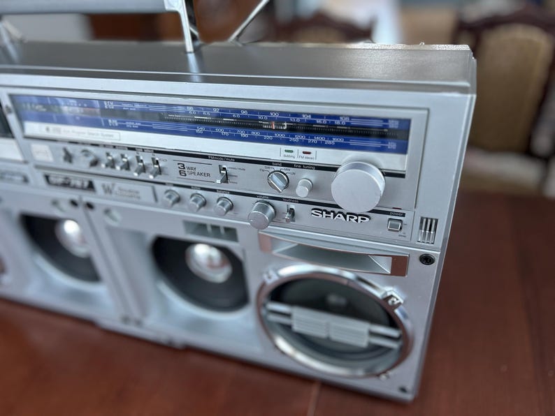 Pu&ograve; includere: Un boombox Sharp color argento caratterizzato da un display di sintonizzazione radio con accenti blu, molteplici manopole di controllo, interruttori e un'etichetta per un sistema a 3 vie e 6 altoparlanti. Il dispositivo audio portatile include una manopola.