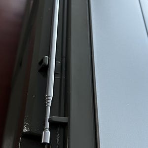 Pu&ograve; includere: Un dispositivo elettronico nero dotato di una lunga e sottile antenna telescopica color argento, retratta e alloggiata in una scanalatura sagomata lungo il lato dell'unit&agrave;. Il dispositivo presenta una finitura nera opaca liscia e un pannello superiore grigio.