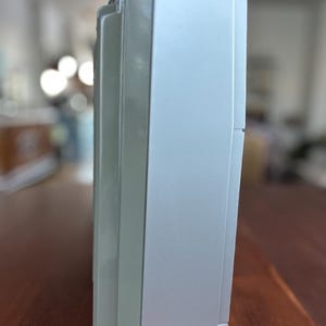 Pu&ograve; includere: Un dispositivo elettronico rettangolare di colore argento con una finitura opaca liscia. Il profilo laterale mostra un orientamento verticale con un pannello leggermente rientrato e una piccola punta di antenna metallica che sporge dal bordo superiore.