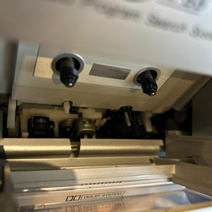 May include: A close-up of a silver cassette player with the cassette door open. The player has two black knobs and the words "Dolby System" are visible. The player is a vintage audio device.
