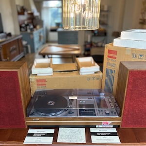 May include: A Sharp brand stereo system featuring a turntable and cassette player with a wood-grain finish, two speakers with red fabric grilles, and a clear plastic dust cover. Includes original cardboard packaging, foam inserts, and instruction manuals.