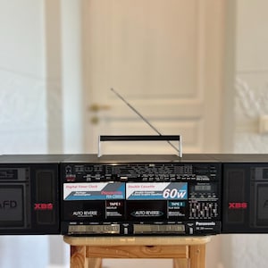 May include: A black Panasonic RX-CW55 portable stereo boombox featuring a double cassette deck, XBS bass system, and an extendable antenna. The front panel displays text including Digital Timer Clock, Auto Reverse, and 60w, with two speakers.