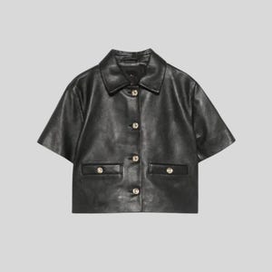 May include: Black short-sleeved jacket with a collared neckline and button-up front. The jacket features two front pockets and gold-colored buttons. The garment is made of a smooth, leather-like material.