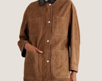May include: A brown suede jacket with a black leather collar. The jacket has four front pockets and white buttons. The sleeves are long, and the jacket appears to be a medium weight. The jacket is a neutral color and could be worn in many settings.