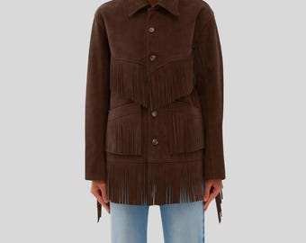Könnte beinhalten: Braune Wildlederjacke mit Fransen. Die Jacke hat eine Knopfleiste, zwei Vordertaschen und Fransen an Brust, Taschen und Saum. Das Model trägt eine hellblaue Jeans.
