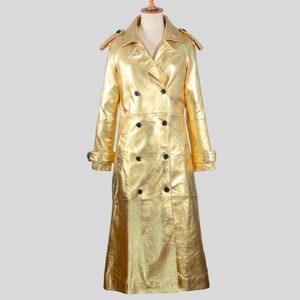 May include: A long gold metallic trench coat with a double breasted closure and a classic collar.