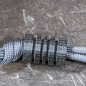 Puede incluir: Primer plano de un cord&oacute;n con estampado en blanco y negro con un tope de cord&oacute;n con estampado en blanco y negro. El cord&oacute;n est&aacute; atado en un nudo y el tope est&aacute; envuelto alrededor del nudo.