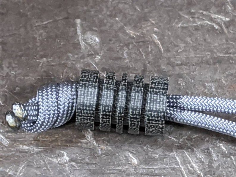 Puede incluir: Primer plano de un cord&oacute;n con estampado en blanco y negro con un tope de cord&oacute;n con estampado en blanco y negro. El cord&oacute;n est&aacute; atado en un nudo y el tope est&aacute; envuelto alrededor del nudo.