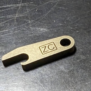 May include: A gold-colored bottle opener with a rounded hole at the top and the letters "ZC" engraved in a square on the handle.