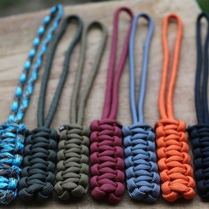 May include: Eight colorful paracord keychains with different knot patterns. The keychains are made with blue, black, green, maroon, gray, orange, and black paracord.