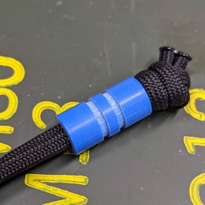 May include: A blue and white paracord bead with a black paracord knot on one end.