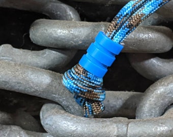 May include: A blue and brown paracord bracelet with a blue plastic bead. The bracelet is wrapped around a chain link.