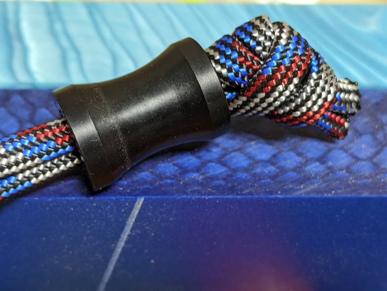 May include: A black plastic cord stop with a braided rope threaded through it. The rope is red, white, and blue.