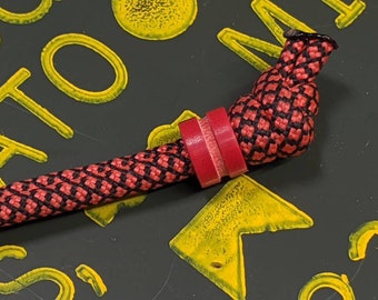 May include: A red and black braided rope with a red plastic bead. The rope is tied in a knot at the end.