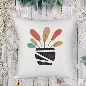 Peut inclure: Un coussin décoratif carré blanc cassé avec un motif de plante brodé. La plante a des feuilles rouges, beiges et turquoise dans un pot à rayures noires et blanches. Le coussin est sur une surface en bois avec des étoiles de mer et un filet décoratif.