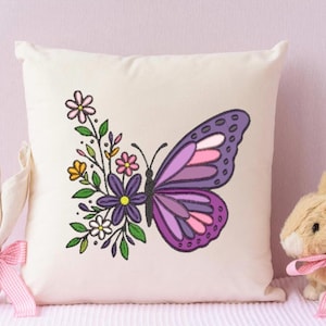Peut inclure: Coussin carré crème avec un motif brodé de papillon et de fleurs. Le papillon a des ailes violettes et roses. Un lapin de Pâques décoratif et un œuf sont sur le côté.