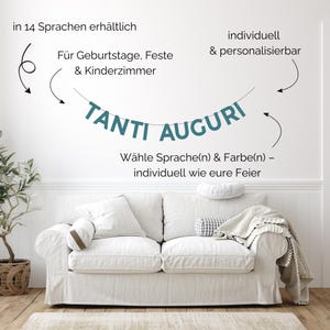 Könnte beinhalten: Ein weißes Sofa mit Kissen und einer Decke steht vor einer weißen Wand. Über dem Sofa befindet sich ein Banner mit der Aufschrift "TANTI AUGURI" in türkisfarbenen Buchstaben. Der Text auf Deutsch besagt, dass das Banner in 14 Sprachen erhältlich ist.